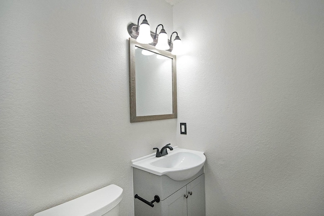 half bathroom featuring toilet, a textured wall, and vanity