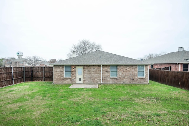 rear view of property featuring a fenced backyard, brick siding, a yard, roof with shingles, and a patio area