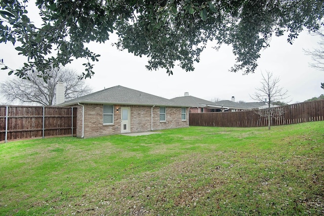 back of house with brick siding, a lawn, a chimney, and a fenced backyard