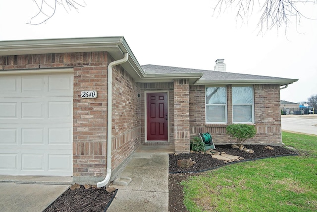 doorway to property with an attached garage, a chimney, and brick siding