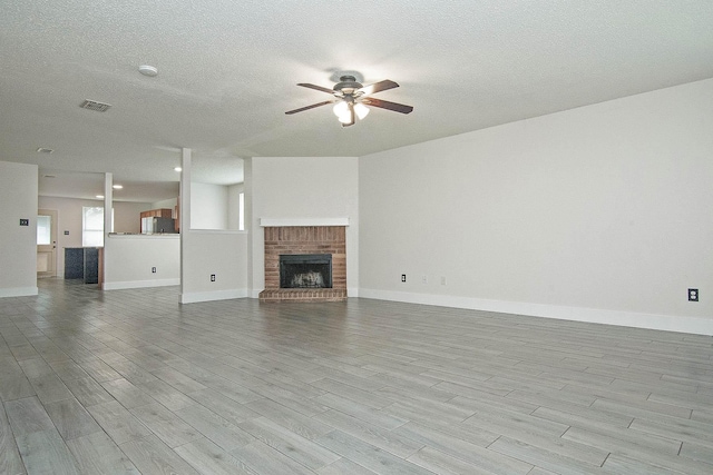 unfurnished living room with visible vents, a ceiling fan, wood finished floors, a textured ceiling, and a fireplace