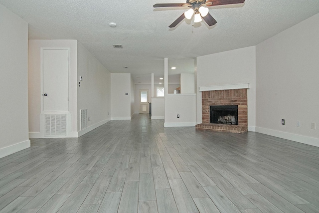 unfurnished living room featuring a textured ceiling, wood finished floors, visible vents, baseboards, and a brick fireplace