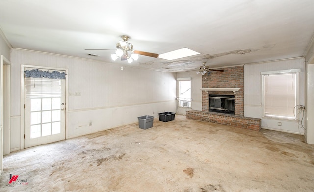 unfurnished living room featuring a skylight, visible vents, a ceiling fan, ornamental molding, and a brick fireplace