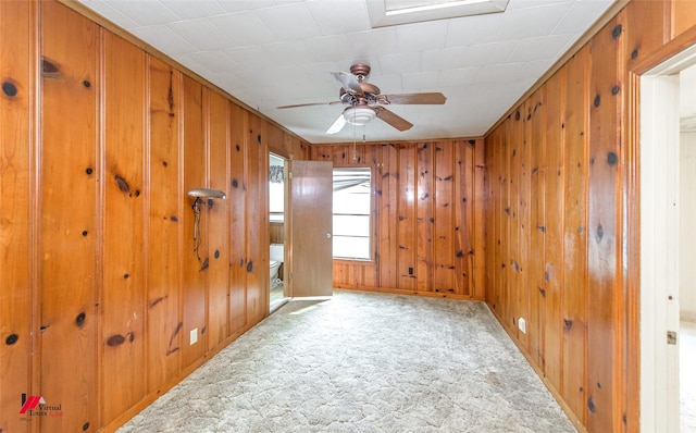 carpeted empty room with wood walls and a ceiling fan