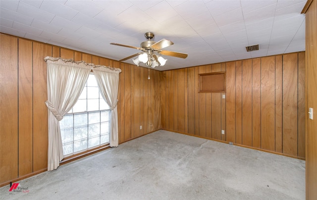 carpeted spare room featuring visible vents, wood walls, and a ceiling fan