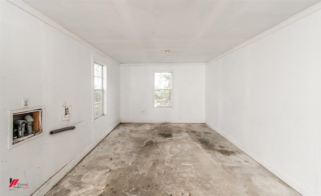 spare room featuring crown molding, baseboards, and unfinished concrete flooring