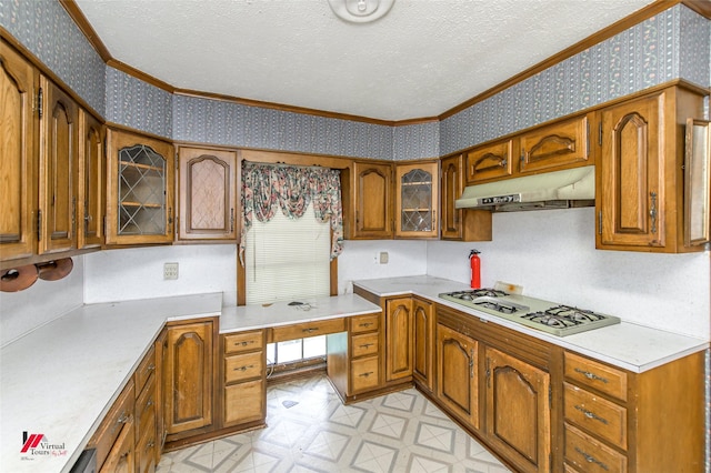 kitchen with wallpapered walls, white gas stovetop, brown cabinets, a textured ceiling, and under cabinet range hood