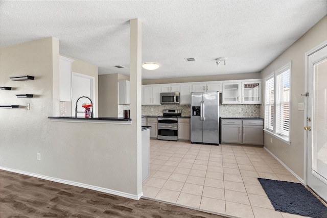 kitchen featuring tasteful backsplash, visible vents, glass insert cabinets, stainless steel appliances, and light tile patterned flooring