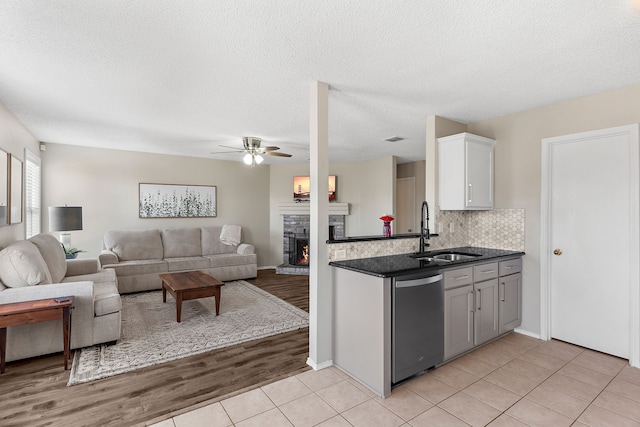 kitchen featuring a warm lit fireplace, stainless steel dishwasher, open floor plan, and a sink