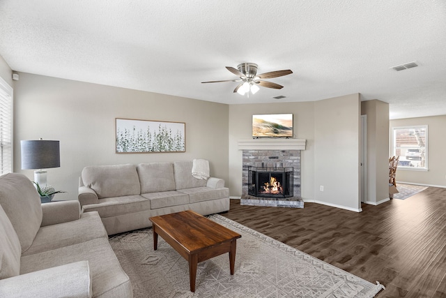 living room featuring visible vents, a brick fireplace, a textured ceiling, wood finished floors, and baseboards