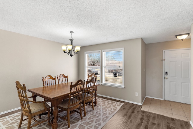 dining space with an inviting chandelier, a textured ceiling, baseboards, and wood finished floors