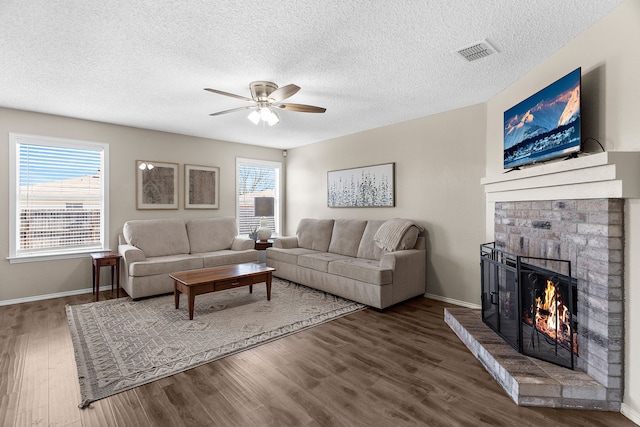 living room featuring ceiling fan, wood finished floors, visible vents, baseboards, and a brick fireplace