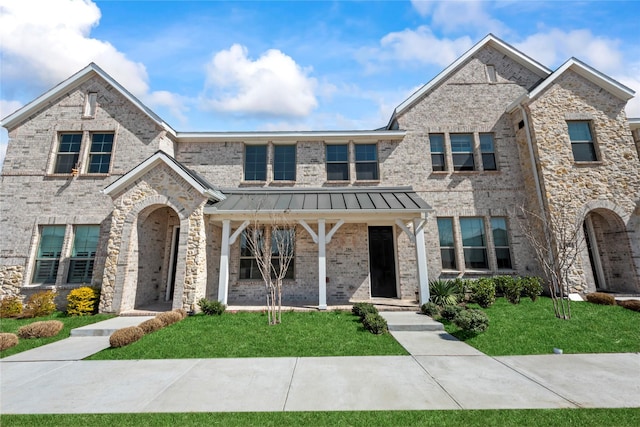 townhome / multi-family property with a standing seam roof, a front yard, metal roof, and brick siding