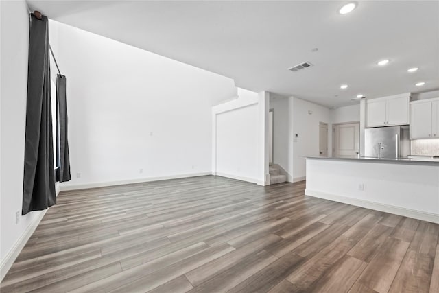 unfurnished living room with light wood-style flooring, stairs, baseboards, and recessed lighting