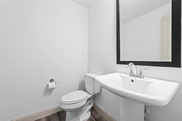 half bath with a sink, wood finished floors, toilet, and baseboards