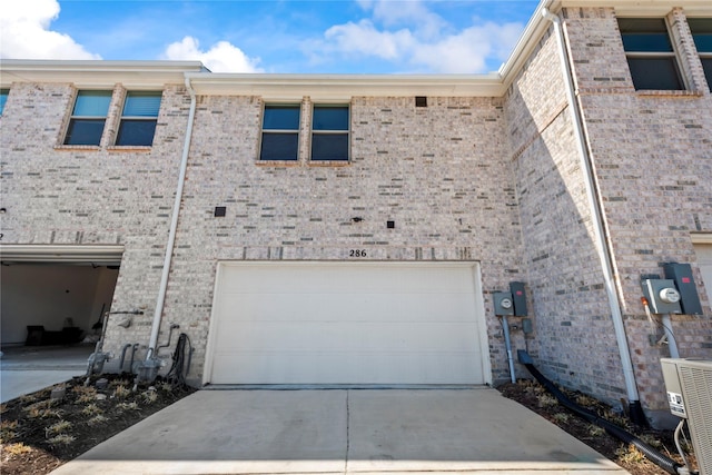 view of side of property featuring brick siding, an attached garage, and central AC unit