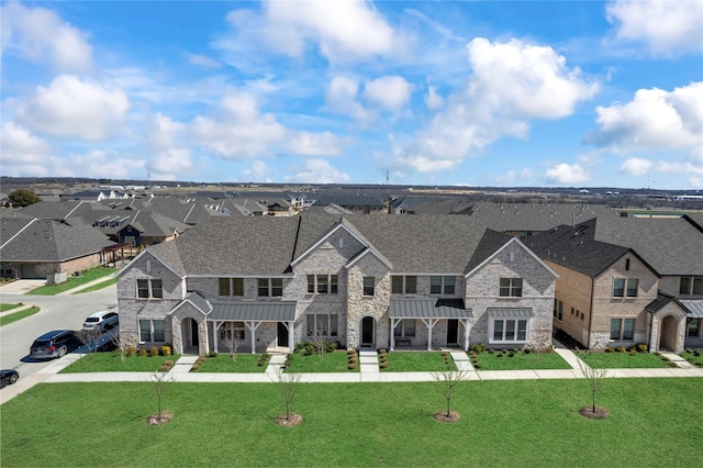 view of front facade with a front yard, a standing seam roof, metal roof, a residential view, and stone siding