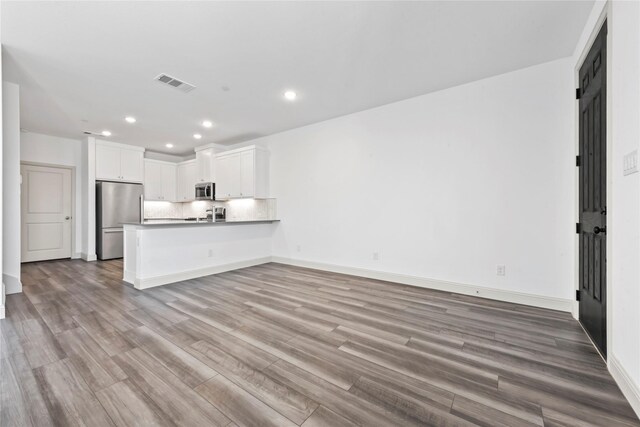 unfurnished living room with a barn door, recessed lighting, wood finished floors, visible vents, and baseboards