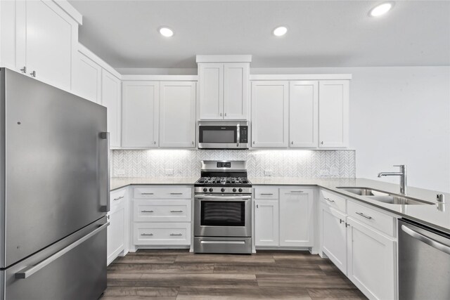 kitchen featuring dark wood finished floors, a sink, stainless steel appliances, white cabinetry, and backsplash