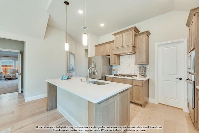 kitchen featuring lofted ceiling, a kitchen island with sink, stainless steel appliances, a sink, and backsplash