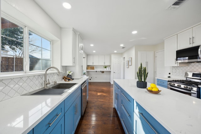 kitchen with appliances with stainless steel finishes, a sink, white cabinetry, and blue cabinets