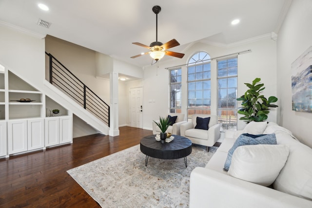 living room with crown molding, visible vents, stairway, dark wood-type flooring, and a ceiling fan