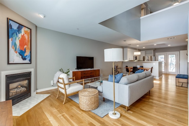 living area featuring visible vents, baseboards, light wood-style flooring, a fireplace with flush hearth, and french doors