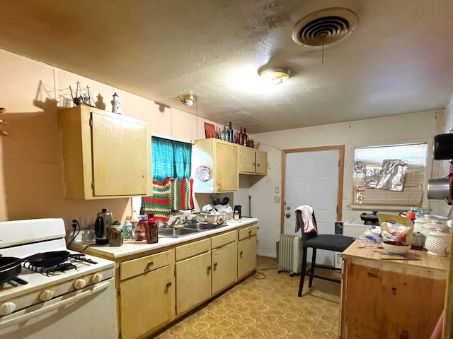 kitchen with white gas stove, radiator, light countertops, visible vents, and a sink