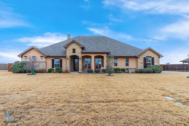 french country home featuring stone siding, a chimney, fence, and a front yard