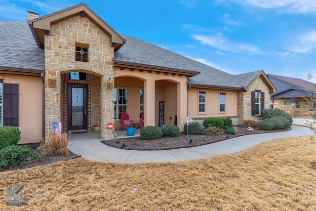 view of front facade featuring stone siding, a shingled roof, and stucco siding