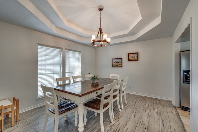 dining room with a tray ceiling, a notable chandelier, light wood-style flooring, and baseboards