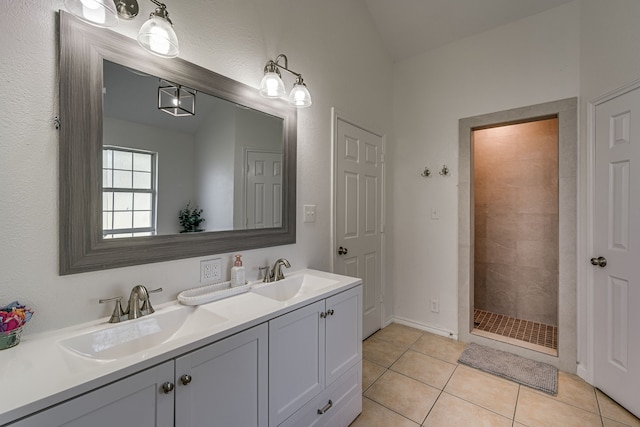 bathroom with double vanity, a tile shower, a sink, and tile patterned floors