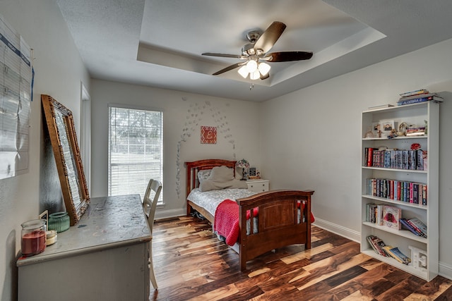 bedroom with a tray ceiling, wood finished floors, and baseboards