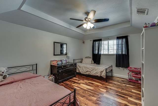 bedroom featuring a raised ceiling, visible vents, baseboards, and wood finished floors