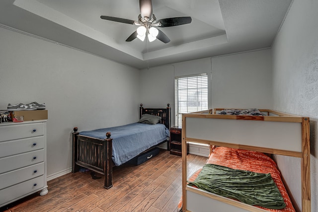 bedroom with a textured wall, a tray ceiling, ceiling fan, and wood finished floors