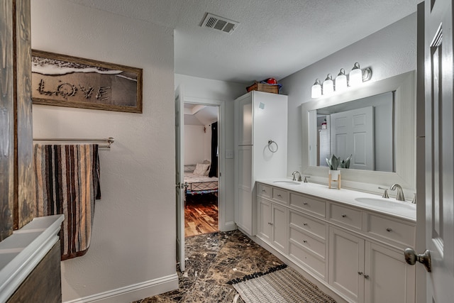 ensuite bathroom featuring double vanity, a textured ceiling, visible vents, and a sink