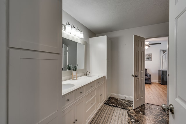 full bath with double vanity, baseboards, marble finish floor, a textured ceiling, and a sink