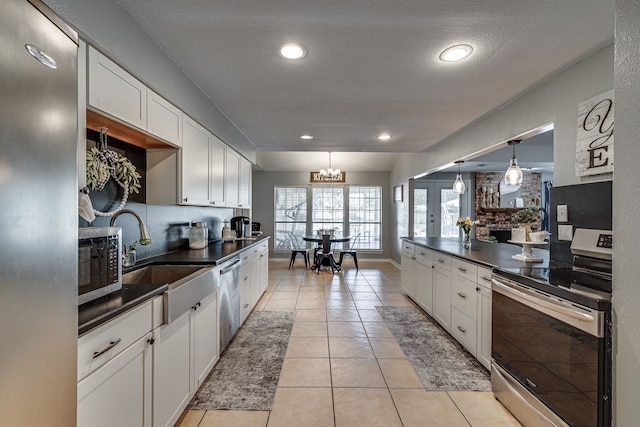 kitchen with light tile patterned floors, dark countertops, stainless steel appliances, white cabinetry, and a sink