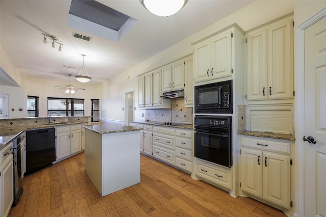 kitchen featuring tasteful backsplash, visible vents, light wood-style floors, under cabinet range hood, and black appliances