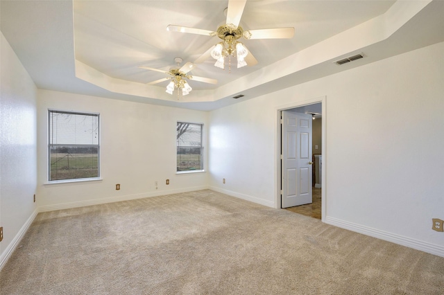 unfurnished room with light colored carpet, a tray ceiling, visible vents, and baseboards