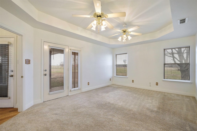 unfurnished room with visible vents, a tray ceiling, a wealth of natural light, and carpet flooring