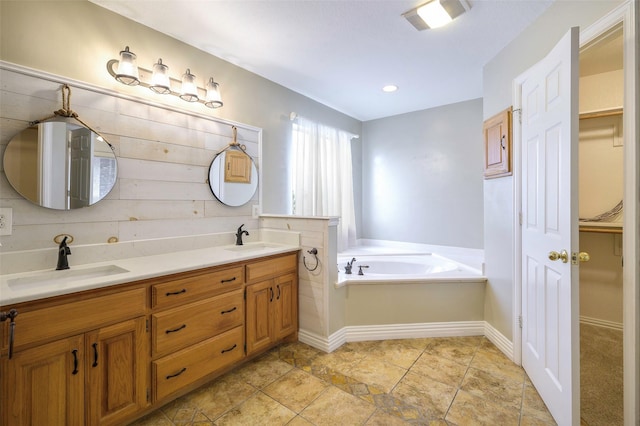 bathroom featuring double vanity, a garden tub, a walk in closet, and a sink