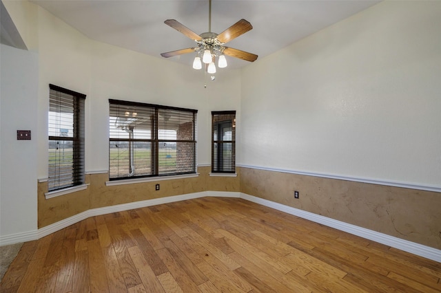 empty room featuring a ceiling fan, wood-type flooring, wainscoting, and baseboards