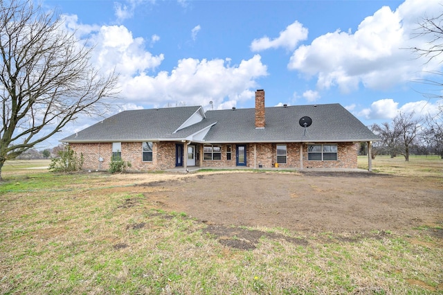 rear view of property with brick siding, a chimney, and a lawn