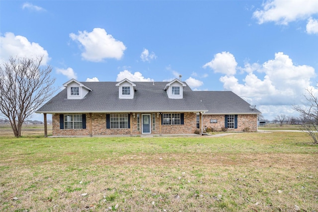 view of front of house with a shingled roof, a front yard, and brick siding