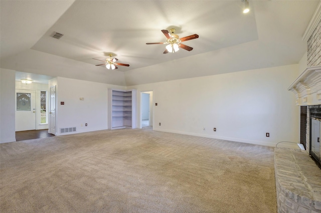 unfurnished living room featuring a brick fireplace, a raised ceiling, visible vents, and light colored carpet