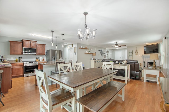 dining room featuring light wood-style floors, a fireplace, and ceiling fan with notable chandelier