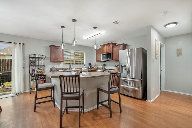 kitchen with stainless steel appliances, visible vents, light wood-style flooring, and a kitchen breakfast bar