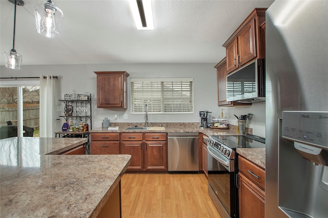 kitchen featuring light stone counters, a sink, light wood-style floors, appliances with stainless steel finishes, and brown cabinets