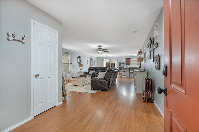 living room with light wood-style flooring, visible vents, baseboards, and a ceiling fan